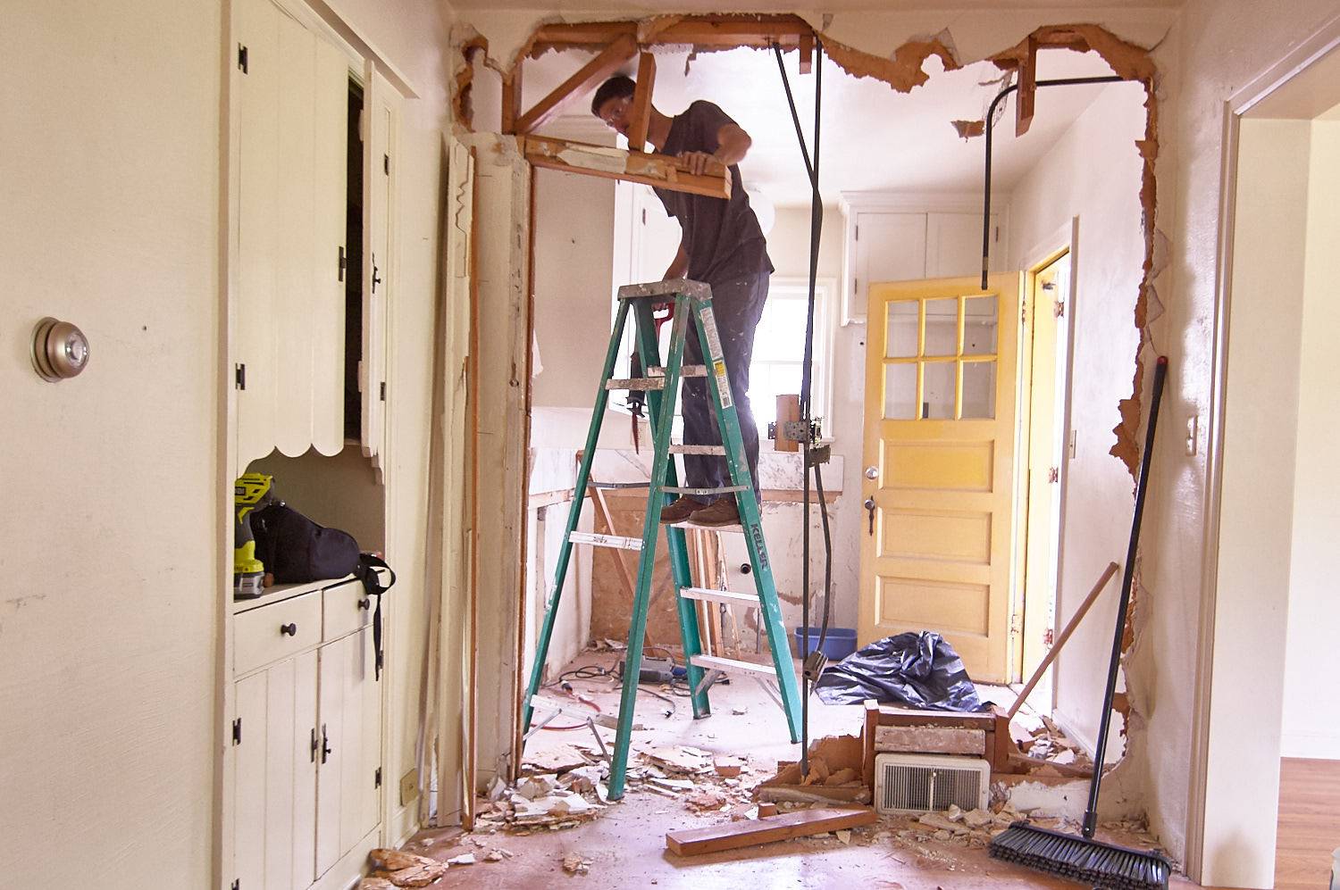 A person is in the ladder and removing doorstep wood with tools.