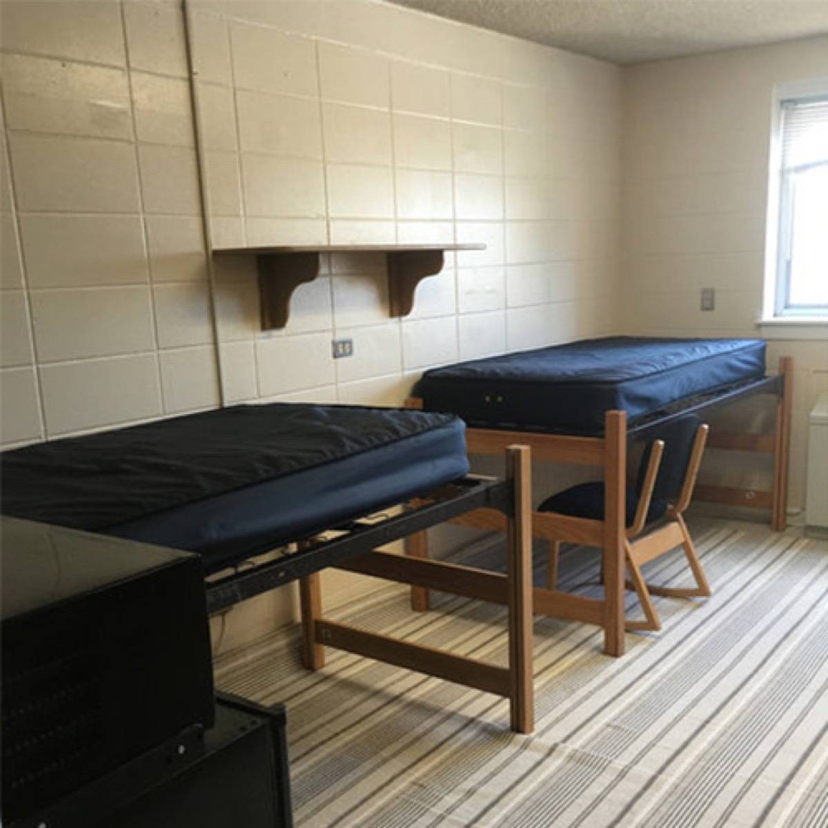 Two wooden beds line near the wall of a room with a wooden chair under it