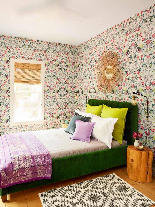 Colorful geometric wallpaper in maximalist design behind green twin bed with brown wood end table.