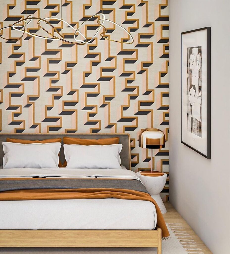 Geometric wallpaper in orange and black behind a white bed and painting on wall.
