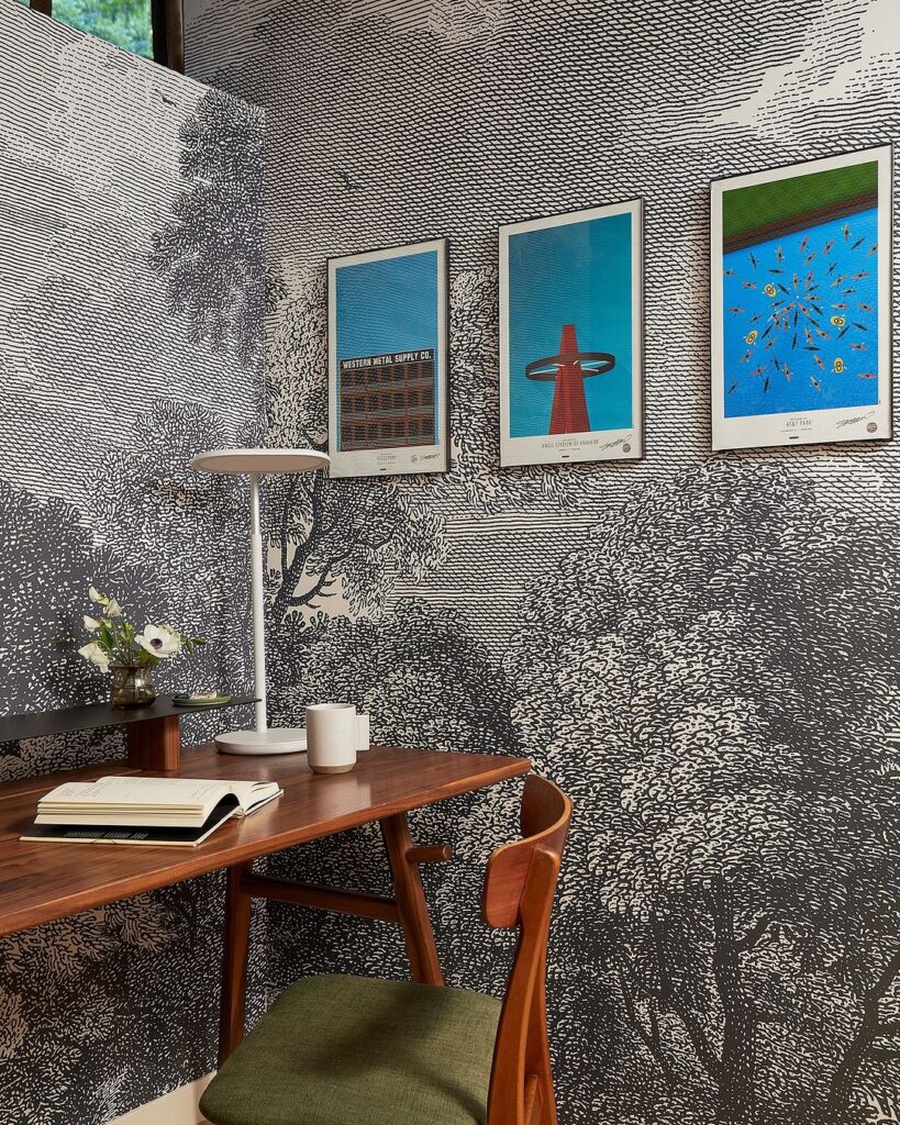 Black and white trees mural wallpaper in office with three painting mounted on the wall and brown office desk.