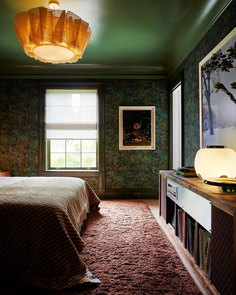 Dark green wallpaper in bedroom with pink floor and bed with brown blanket.