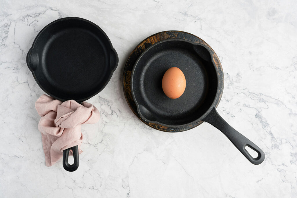 Two cast iron pans, one with an egg in it.